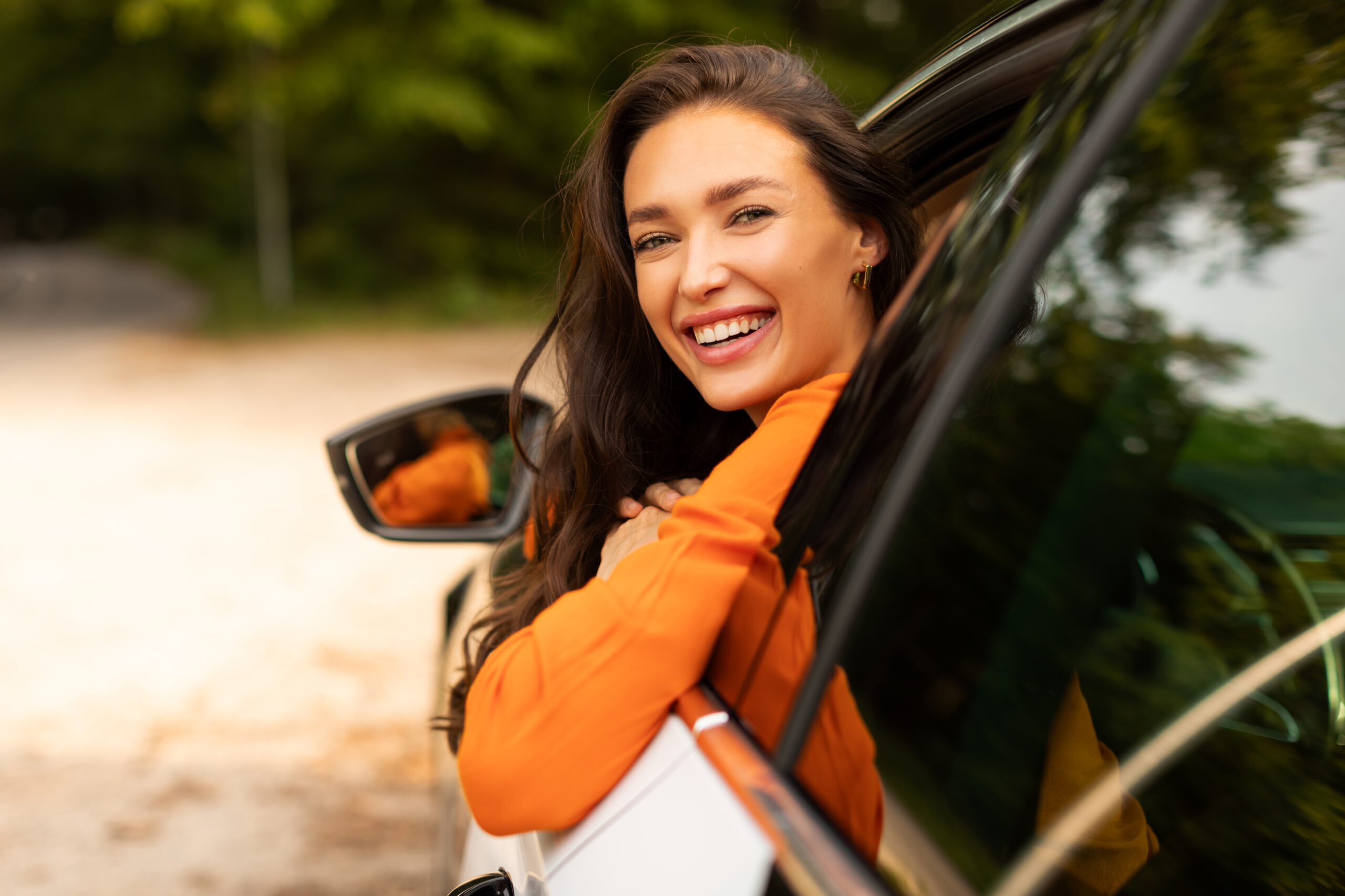 Charming lady looking out of window and smiling, sitting on drivers seat in her new automobile, enjoying road trip alone